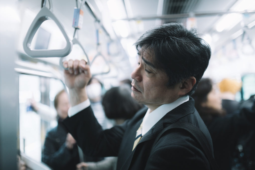 電車のつり革を握って寝てしまっている男性